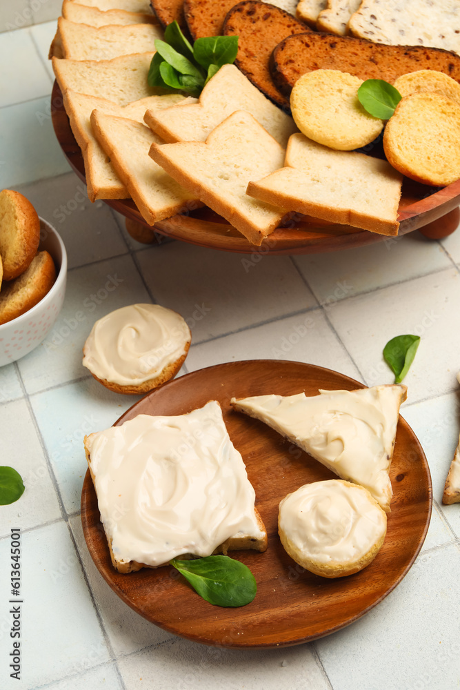 Plate of tasty toasts and croutons with cream cheese on white tile background