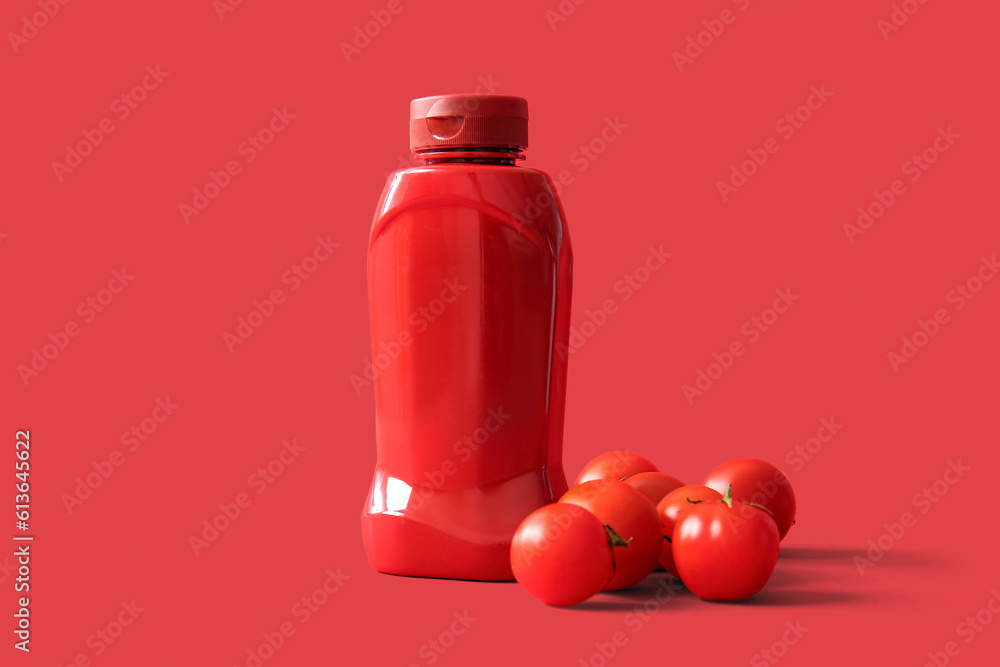 Bottle of ketchup and tomatoes on red background