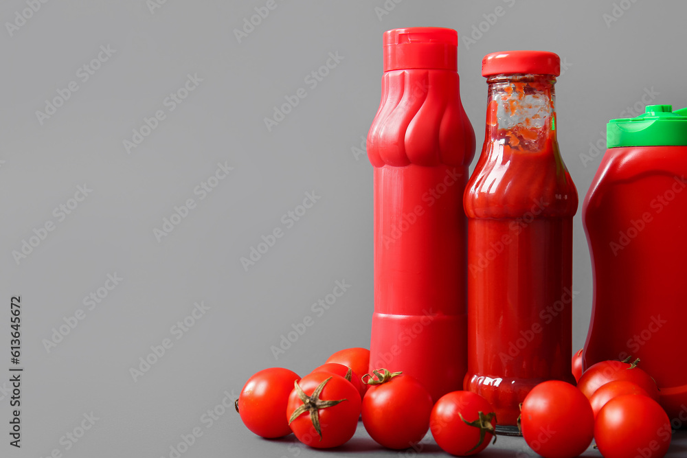 Bottles of ketchup and tomatoes on grey background