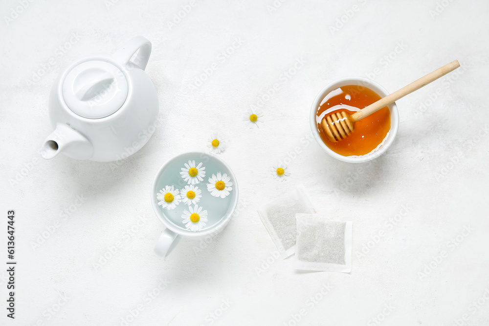 Composition with teapot, cup of water, chamomile flowers, honey and tea bags on light background