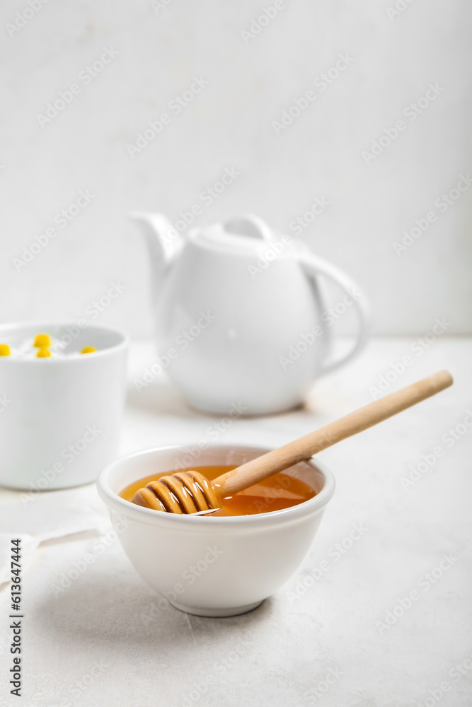 Bowl of honey, teapot and cup with chamomile flowers on light background