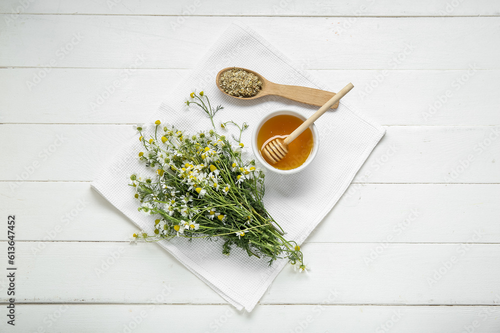 Bowl of honey, fresh and dried chamomile flowers on light wooden background