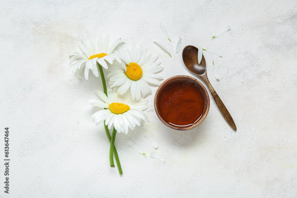 Bowl of honey, spoon and beautiful chamomile flowers on light background