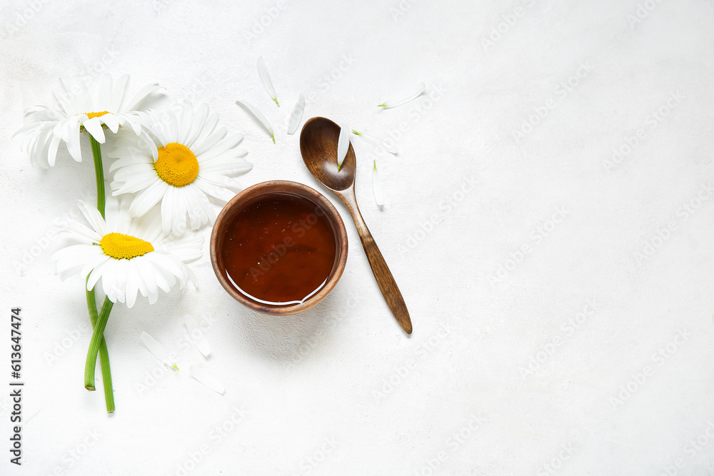 Bowl of honey, spoon and beautiful chamomile flowers on light background