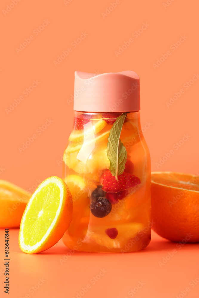 Sports bottle of infused water with different sliced fruits on orange background