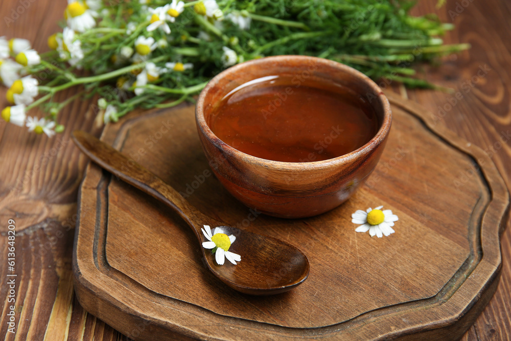 Board with bowl of honey and fresh chamomile flowers on wooden background, closeup