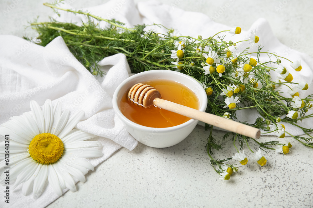 Bowl of honey and fresh chamomile flowers on light background