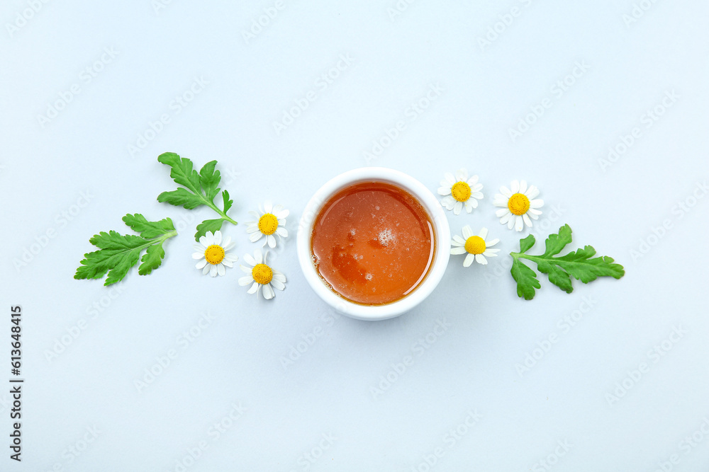 Composition with bowl of honey, chamomile flowers and leaves on light background