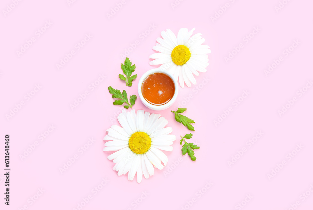 Composition with bowl of honey, chamomile flowers and leaves on pink background