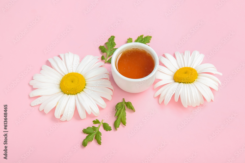 Composition with bowl of honey, chamomile flowers and leaves on pink background