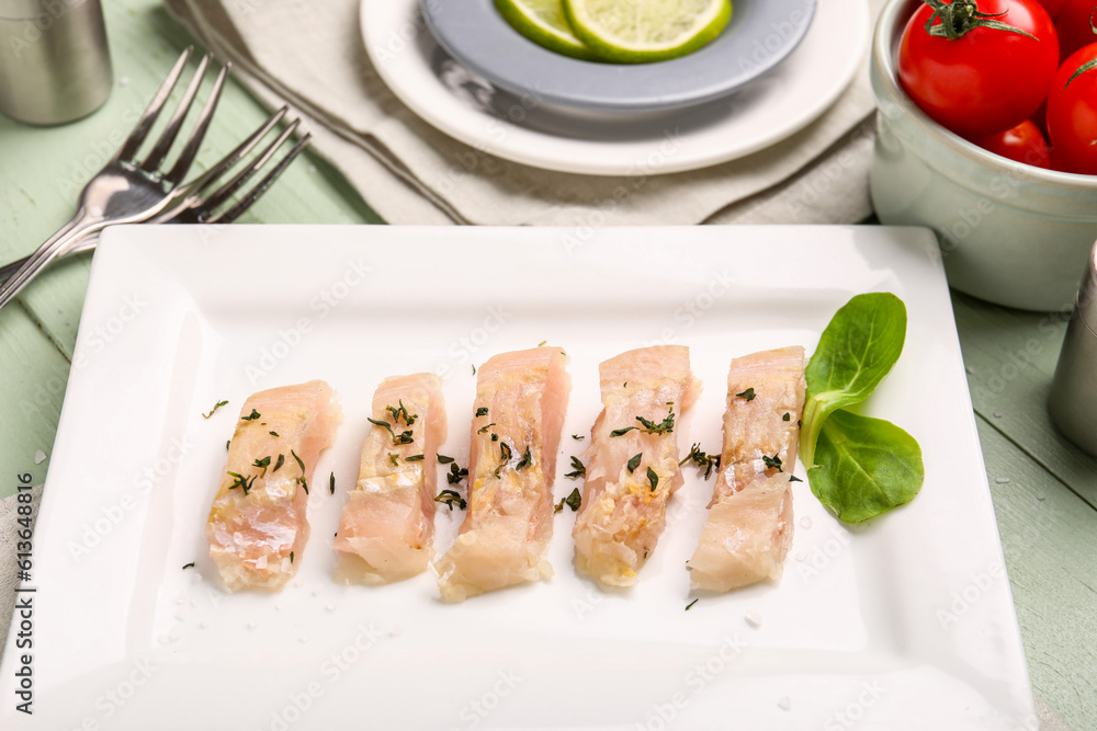 Plate with pieces of raw codfish fillet on green wooden background