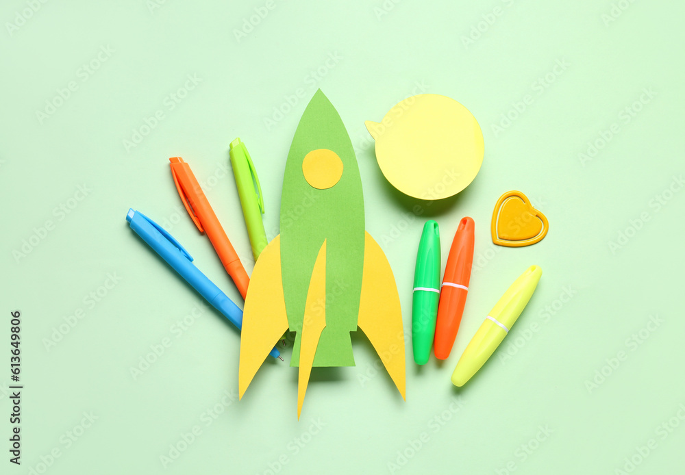 Paper rocket with different stationery and speech bubble on green background