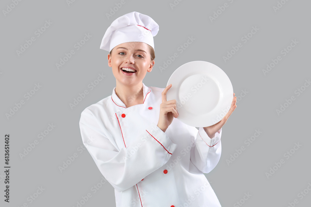 Female chef with empty plate on grey background