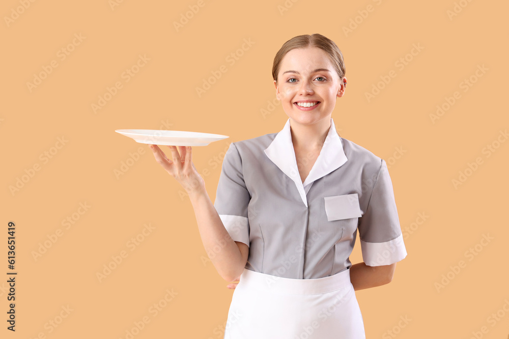 Young waitress with empty plate on beige background