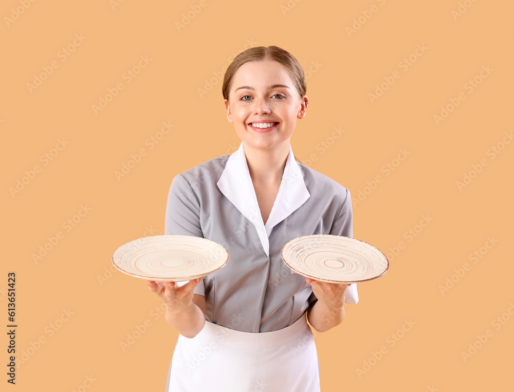 Beautiful young waitress with empty plates on beige background