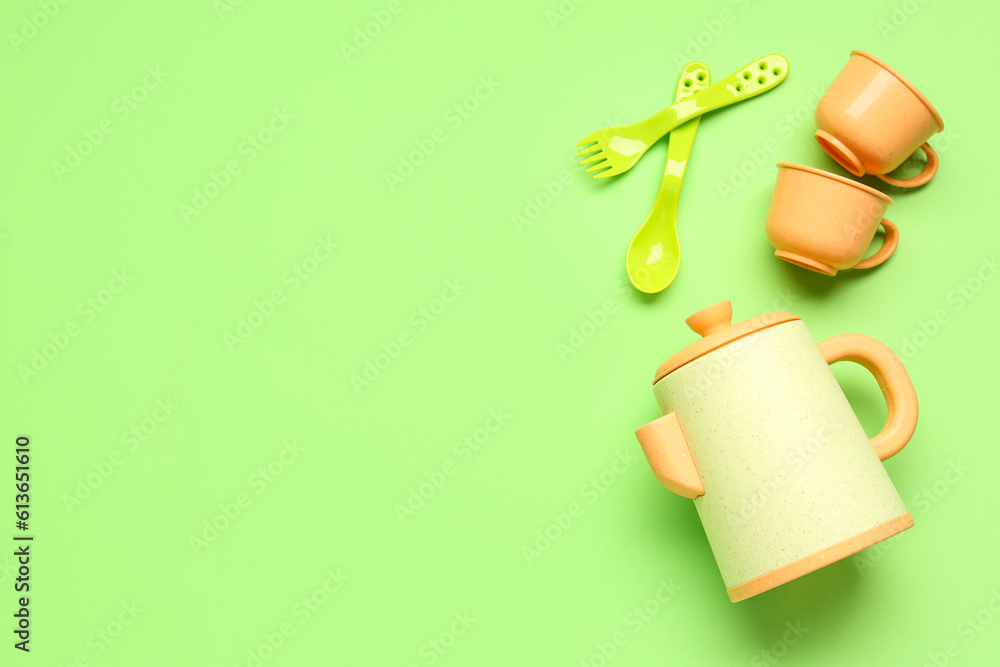 Teapot with cups and cutlery for baby on green background