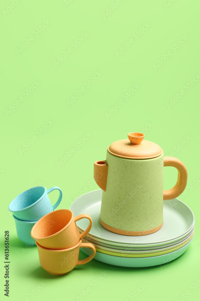 Teapot with cups and plates for baby on green background