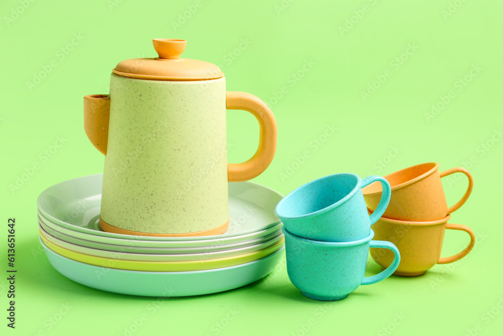 Teapot with cups and plates for baby on green background