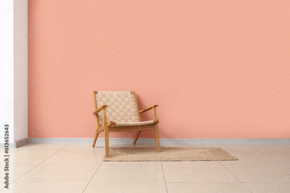 Cozy armchair and wicker rug near pink wall