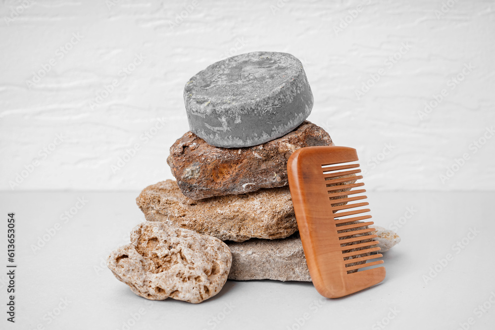 Grey solid shampoo bar with stones and comb on table near white wall