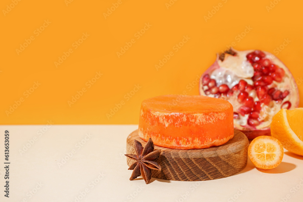 Wooden stand with solid shampoo bar with orange, kumquat and pomegranate on table near orange wall