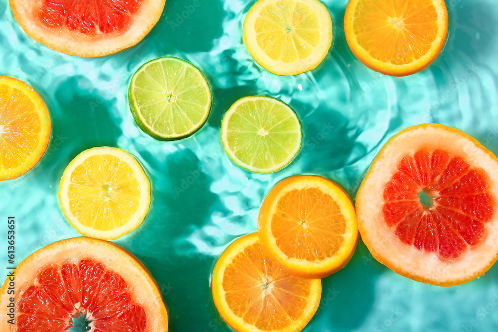 Different citrus fruit slices in water on turquoise background