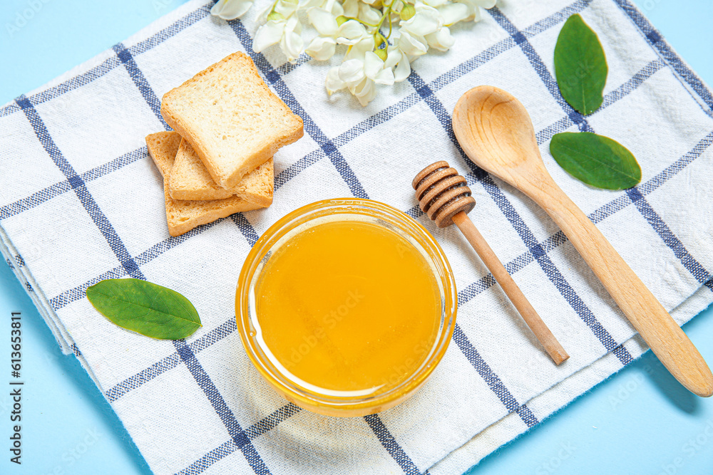 Bowl of honey with flowers of acacia and crackers on blue background, closeup