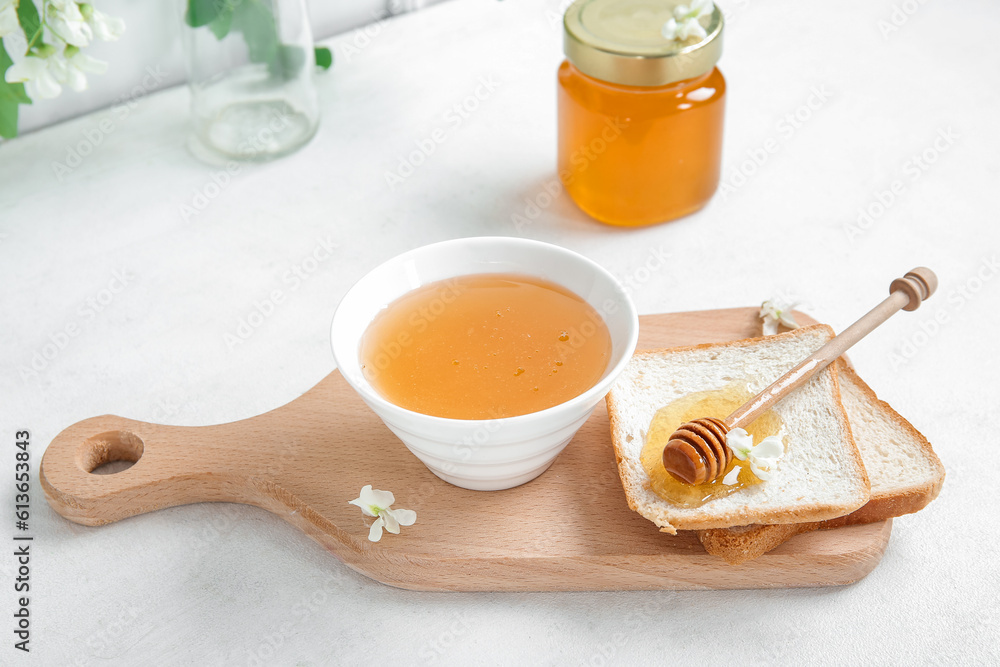 Bowl of honey with flowers of acacia and toasts on light background, closeup