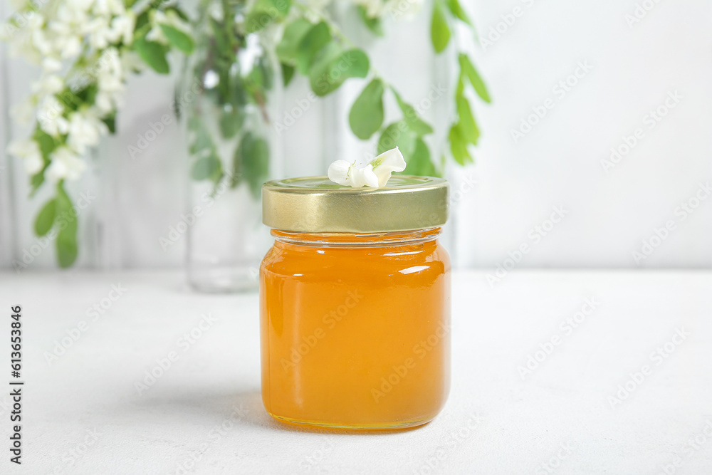 Jar of honey with flowers of acacia on light background, closeup