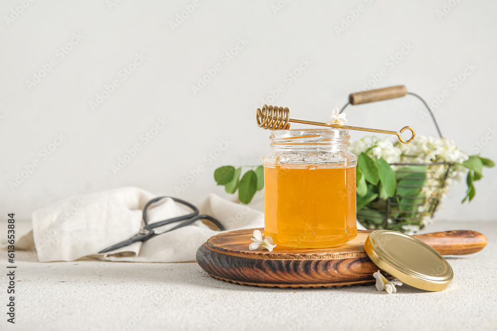 Jar of honey with flowers of acacia and dipper on light background