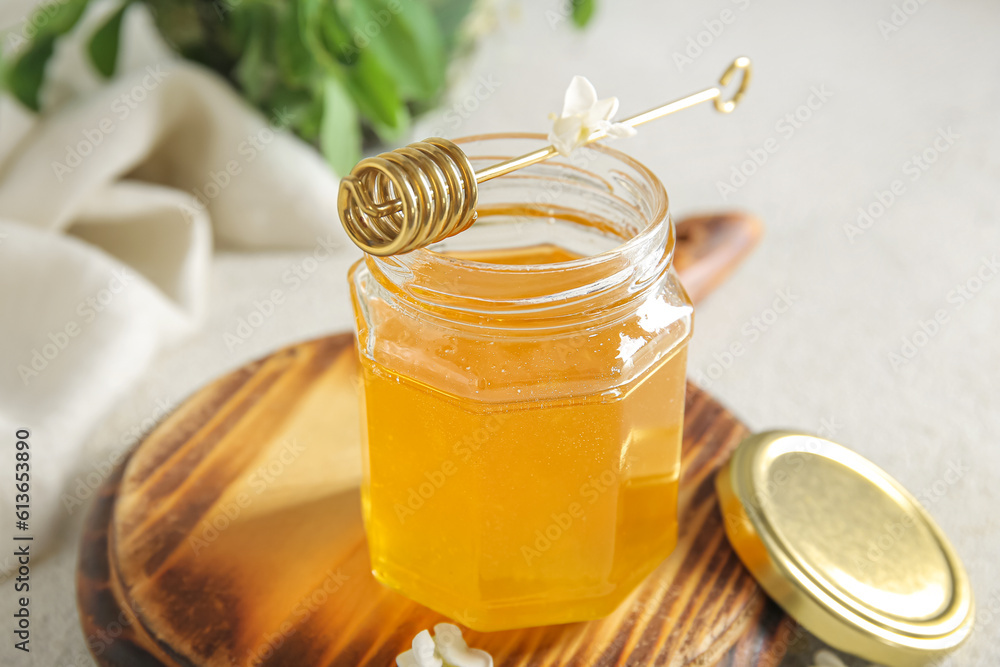 Jar of honey with flowers of acacia and dipper on table, closeup