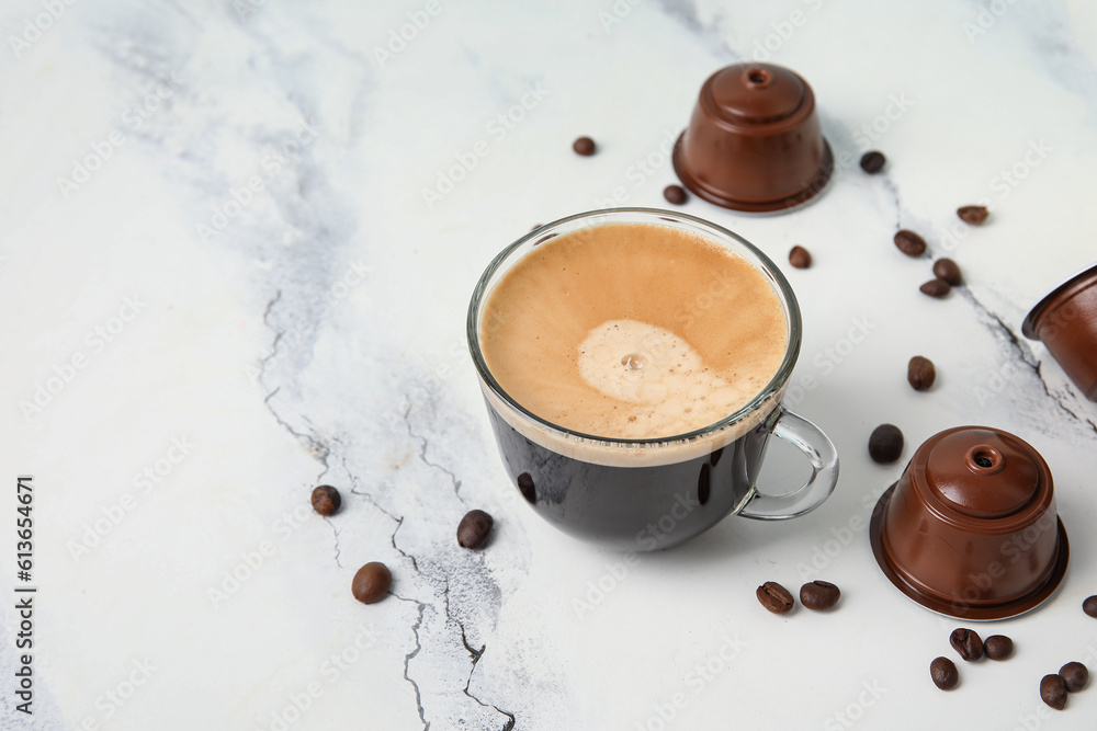 Cup of delicious espresso, pods and beans on white table