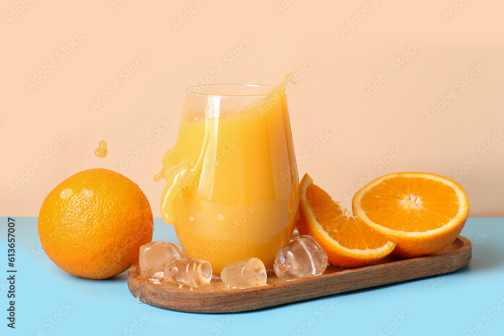 Board and glass of fresh orange juice with splashes on table against beige background