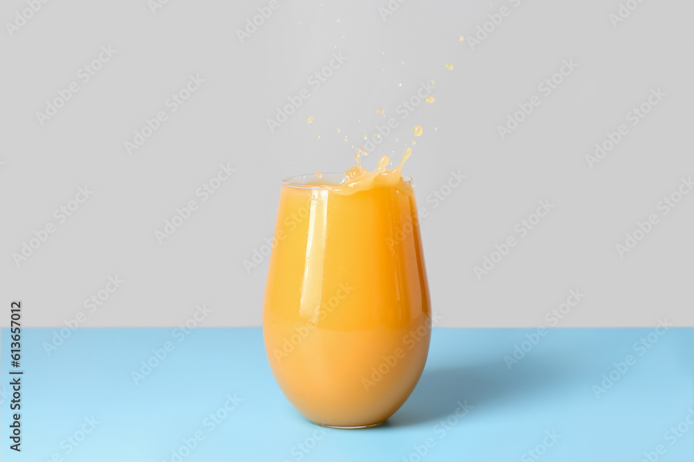 Glass of fresh orange juice with splashes on table against grey background