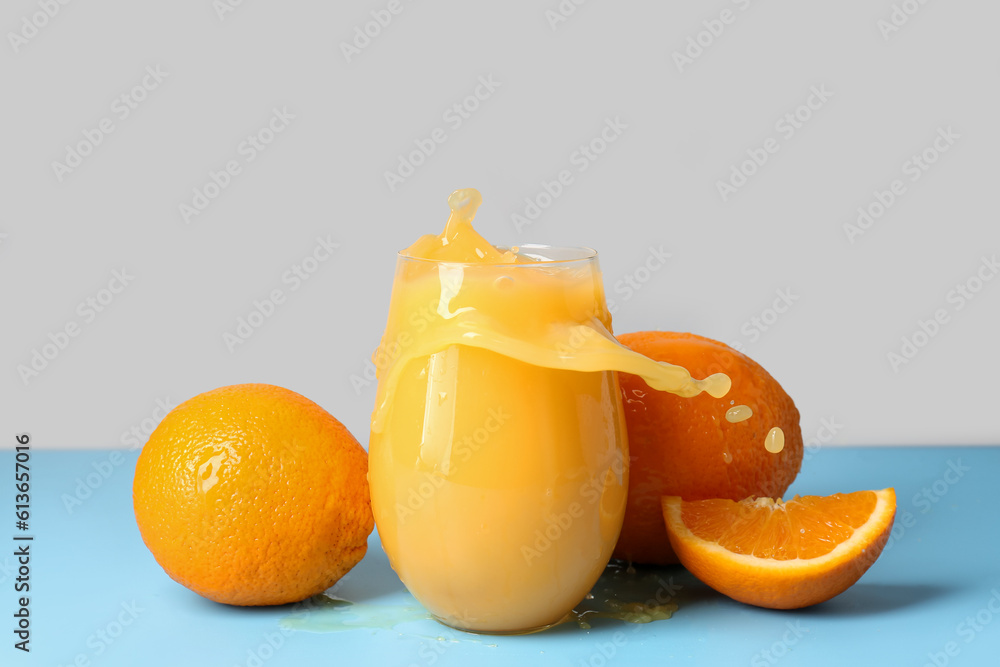 Glass of fresh orange juice with splashes on table against grey background