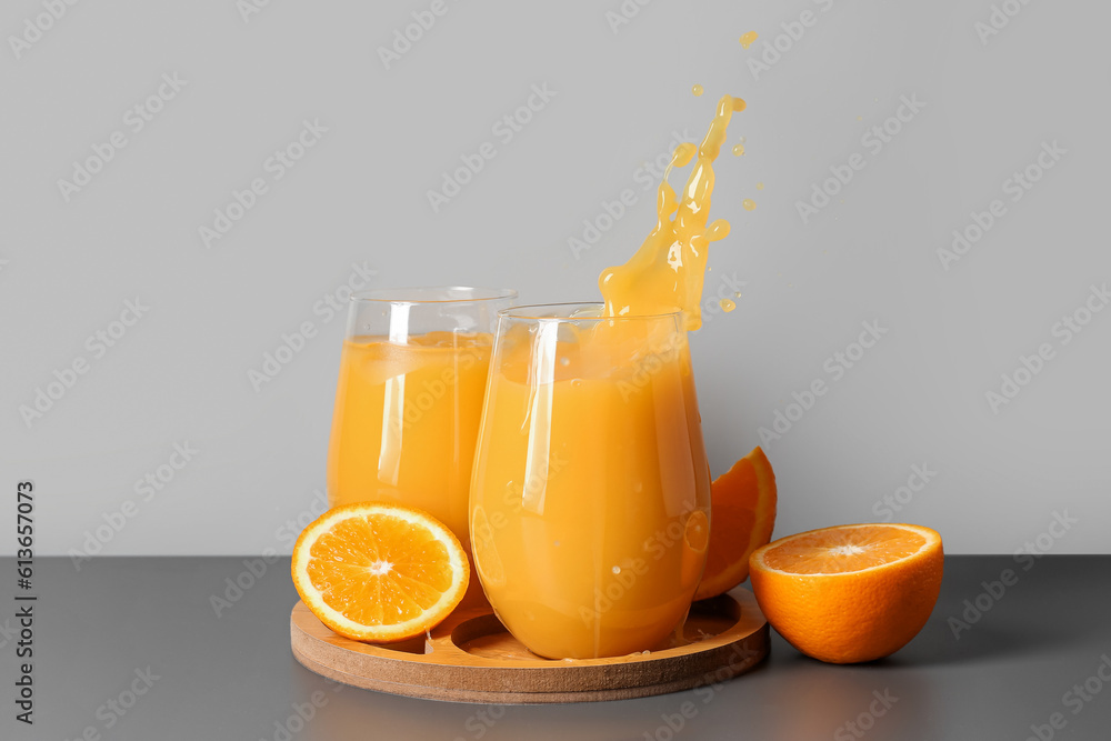 Board and glasses of fresh orange juice with splashes on table against grey background