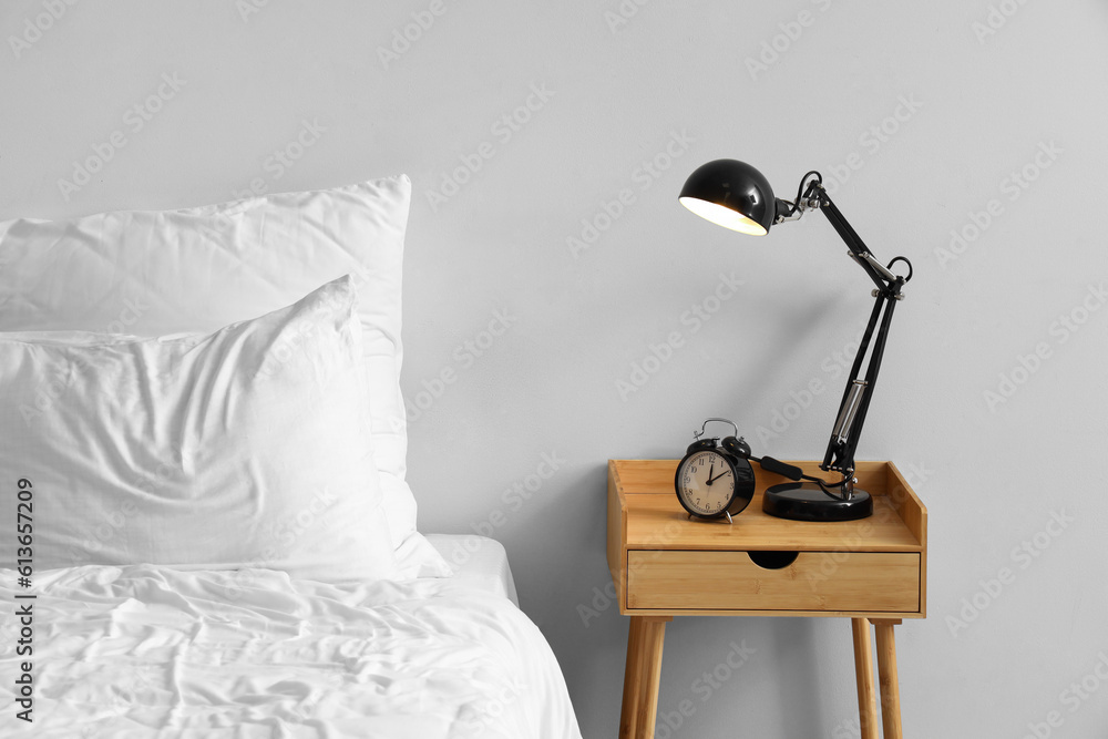 Alarm clock with glowing lamp on table in light bedroom