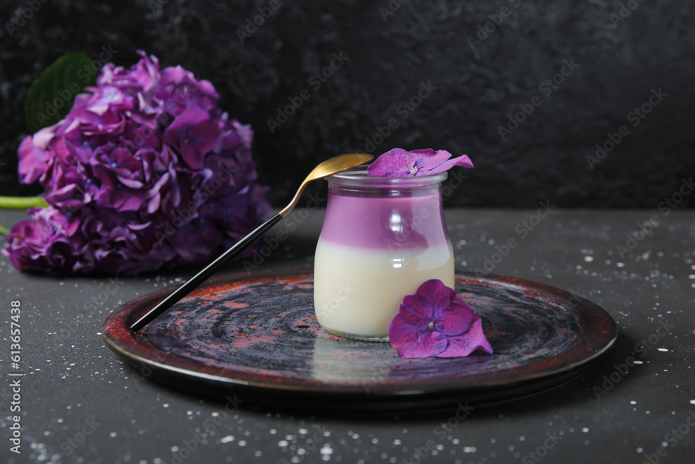 Glass of panna cotta with beautiful hydrangea flowers on black table