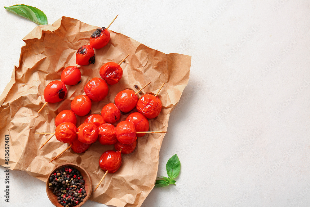 Baking paper and skewers with tasty grilled tomatoes on white background