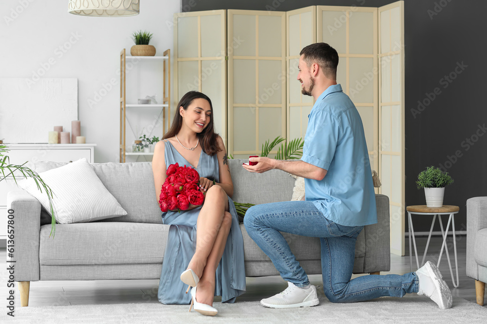 Young man proposing to his girlfriend with flowers at home