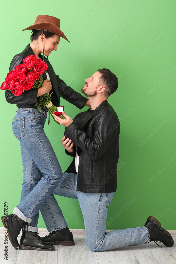 Young man proposing to his girlfriend near green wall