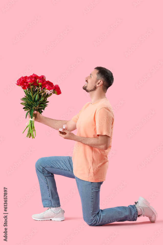 Young man with engagement ring and flowers on pink background