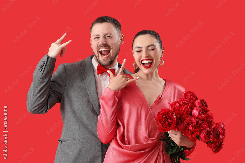 Happy engaged couple with flowers showing  devil horns  on red background