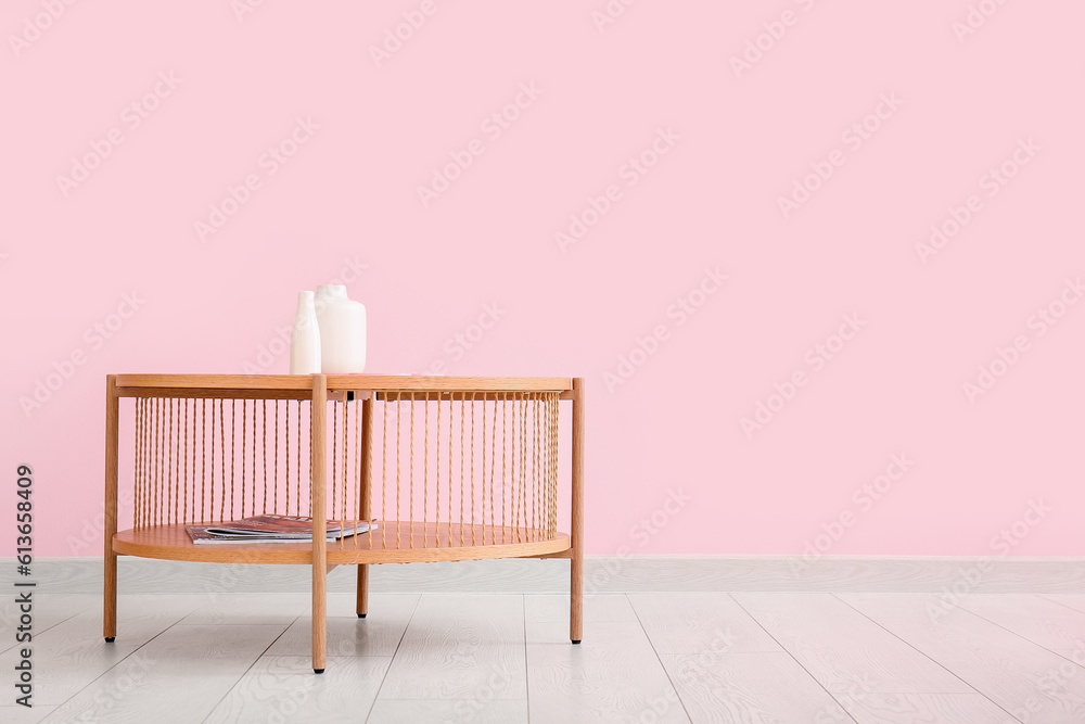 Wooden coffee table with vases and magazines near pink wall