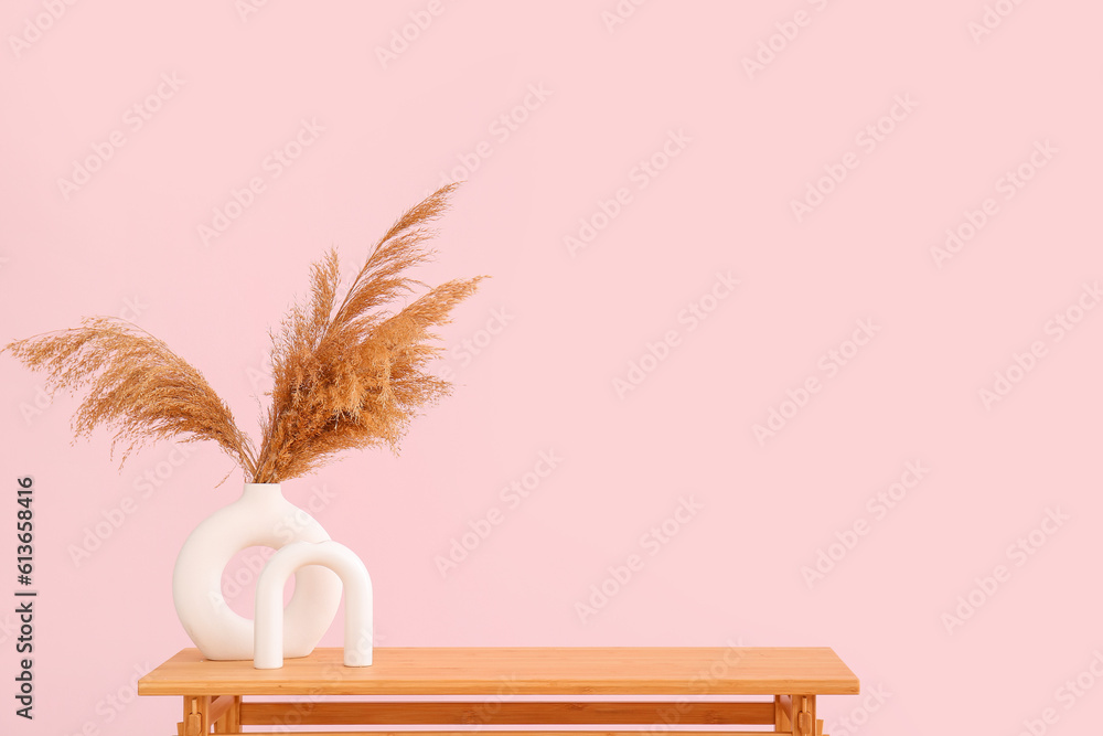 Wooden table with pampas grass in vase near pink wall