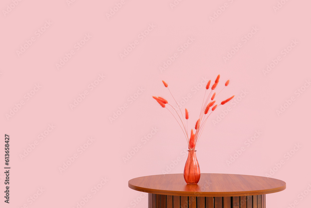 Wooden coffee table with red lagurus grass in vase near pink wall