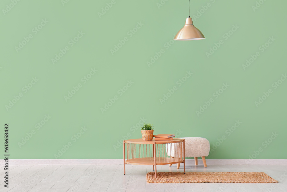 Wooden coffee table with houseplant, books, lamp and pouf near green wall