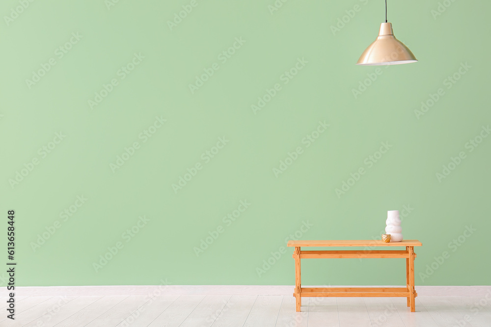 Wooden table with vase and cup near green wall