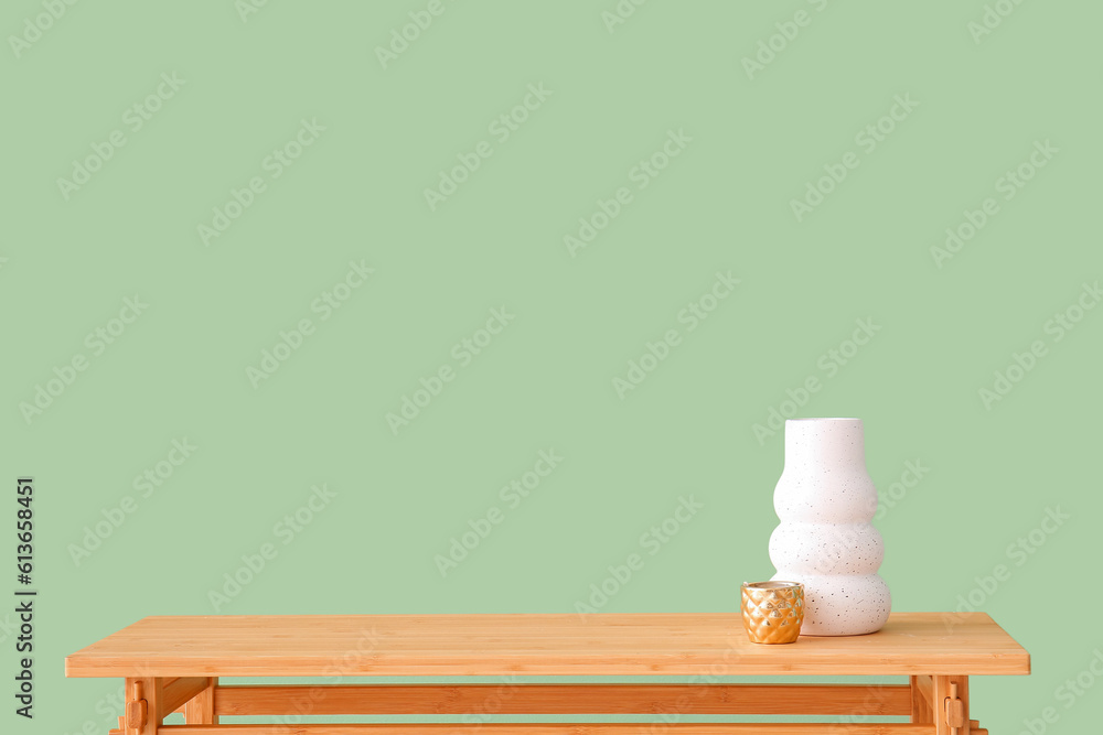 Wooden table with vase and cup near green wall