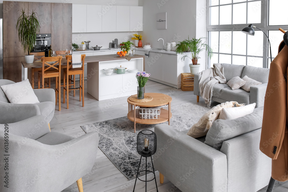 Interior of light open plan kitchen with grey sofas and armchairs